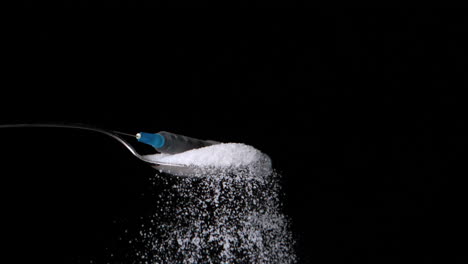 syringe falling onto spoon full of sugar on black background