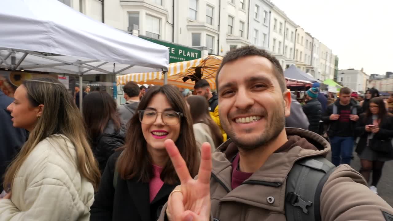 Happy couple filming themselves walking through Portobello Road Market, London. Handheld