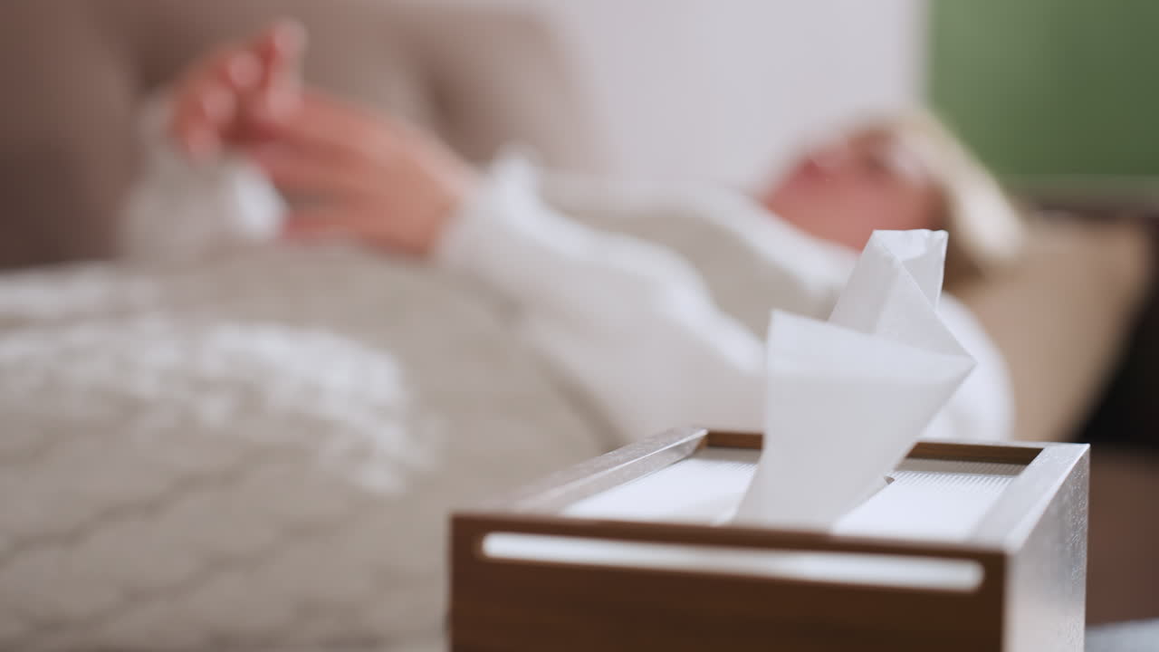 Tissue box on table in restorative room with blurred young woman lying in recliner moving hands gently conveying comfort and support in counseling environment under soft warm therapeutic lighting