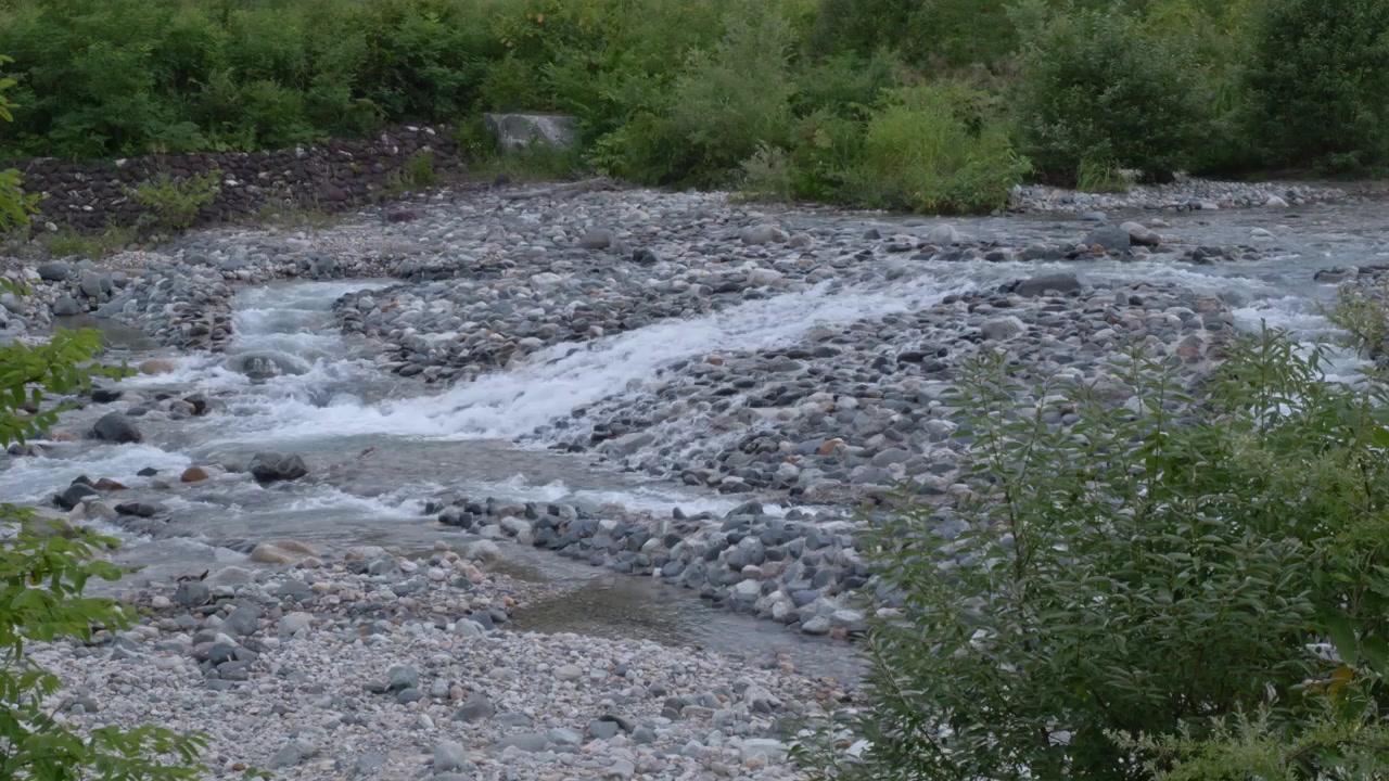 Río de montaña con lecho rocoso y poco profundo lleno de grava y piedras. - Plano general