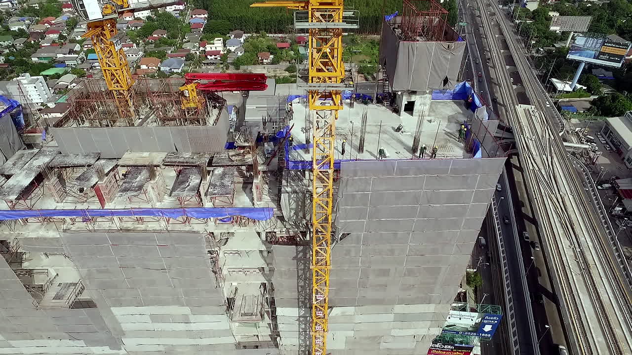 Aerial view of a building construction site with workers assembling the structural framework, machinery in operation, and materials arranged across the work area in an active urban project