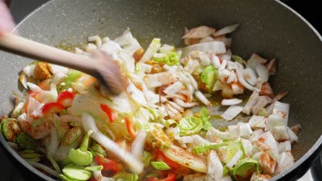 cooking and stirring chopped vegetables and chicken breast seasoned with spices