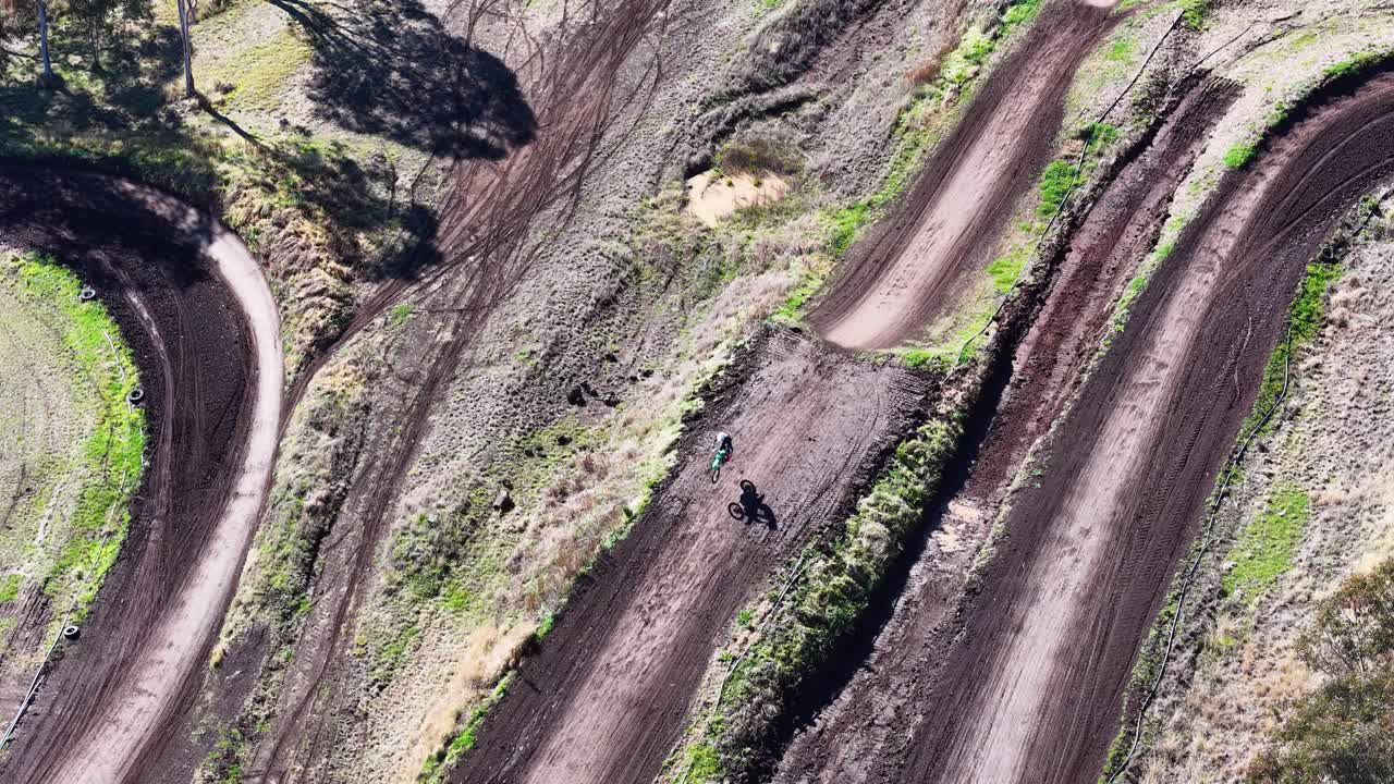 Motocross rider navigates winding dirt track, aerial perspective, bright daylight, dynamic camera movement