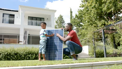 african american father and son examine a solar panel outdoors at home