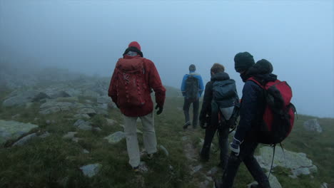 eine gruppe von bergsteigern wandert im morgennebel mit rucksack auf gras und felsen, abenteuer schweizer alpen