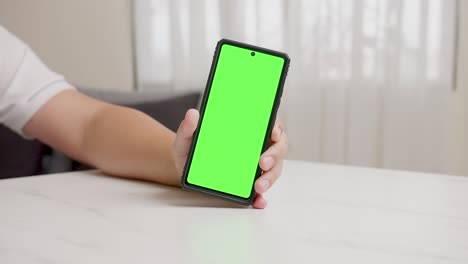 Man's-hand-shows-mobile-smartphone-with-green-screen-in-vertical-position-isolated-on-green-background