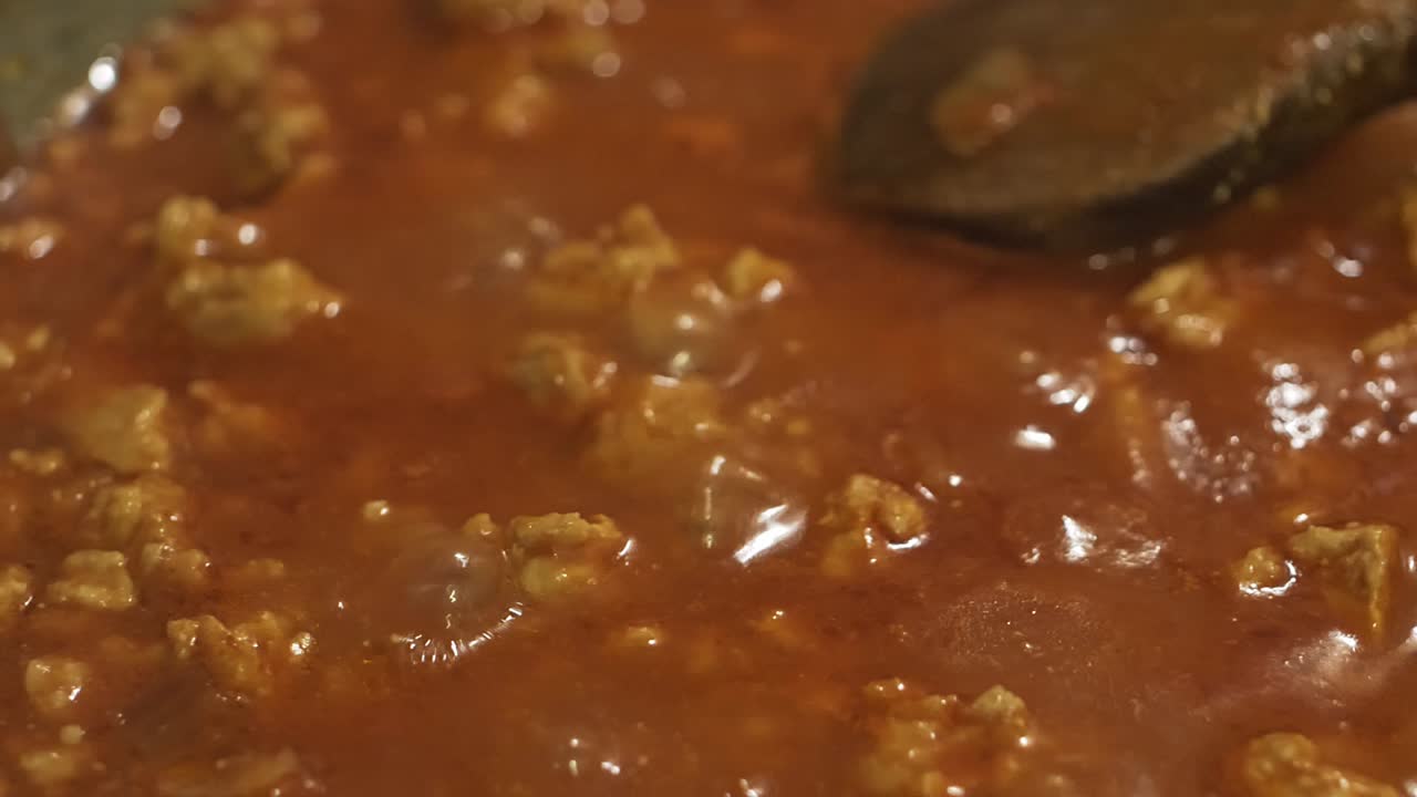 Classical bolognese sauce cooking closeup. Slow motion camera pan from left to right over the boiling meal.