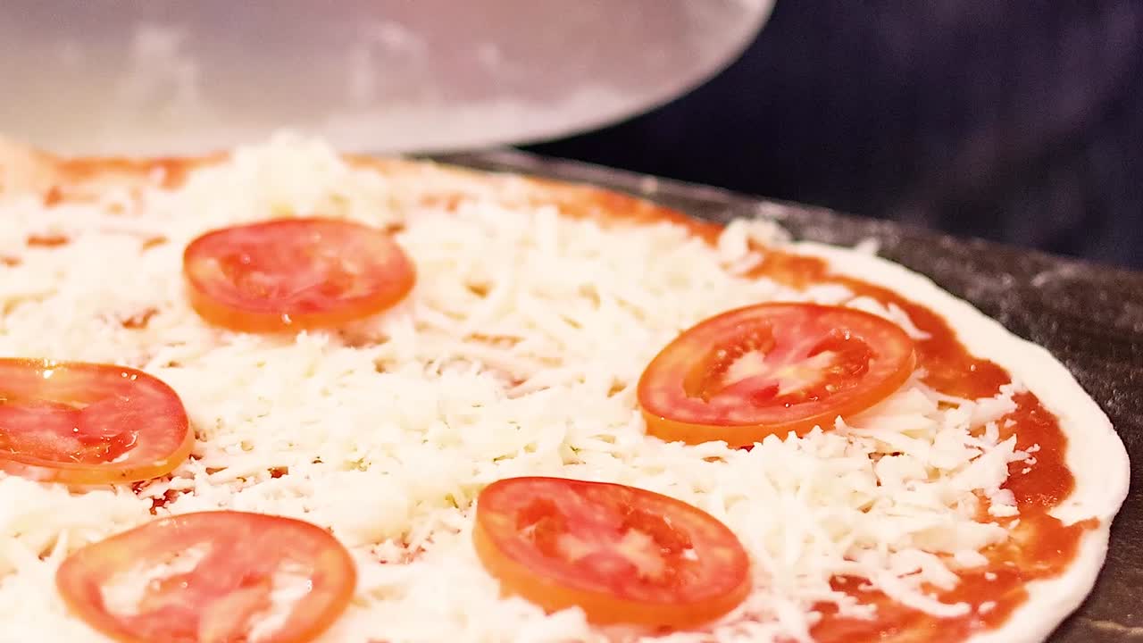 A detailed view of a pizza being prepared with tomato slices and cheese on a wooden surface.