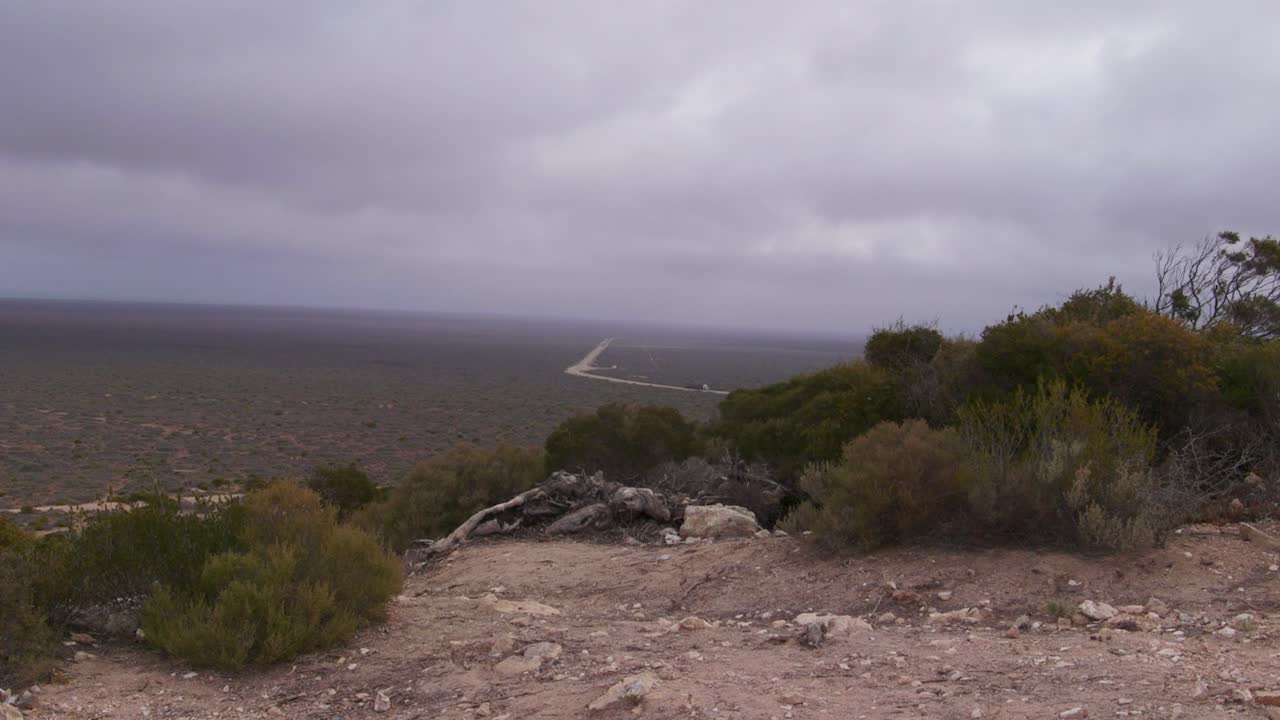 A remote road stretches through a vast desert under a moody cloudy sky
