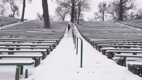 young man with red hoodie and black pants is running up stairs outside in the amphitheater in winter