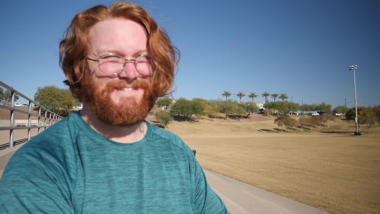 un hombre pelirrojo se ríe mientras está sentado en un parque en un día soleado.