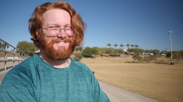 A red hair man laughs while sitting in a park on a sunny day.