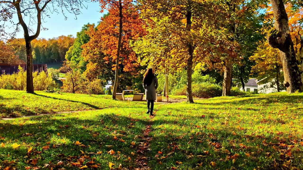 Woman strolls in Cesis park with autumn colors, peaceful and vibrant scene