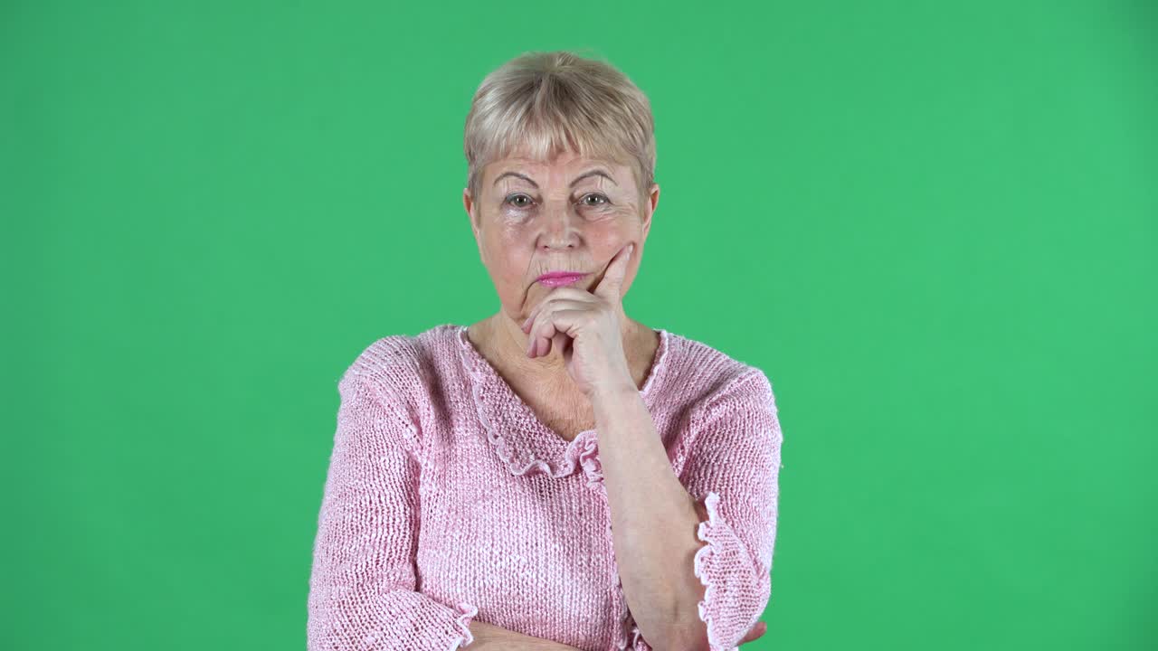 Ritratto di donna anziana che pensa con concentrazione, turbata, senza idee. Nonna dai capelli grigi con capelli corti e un maglione rosa su schermo verde in studio. Primo piano