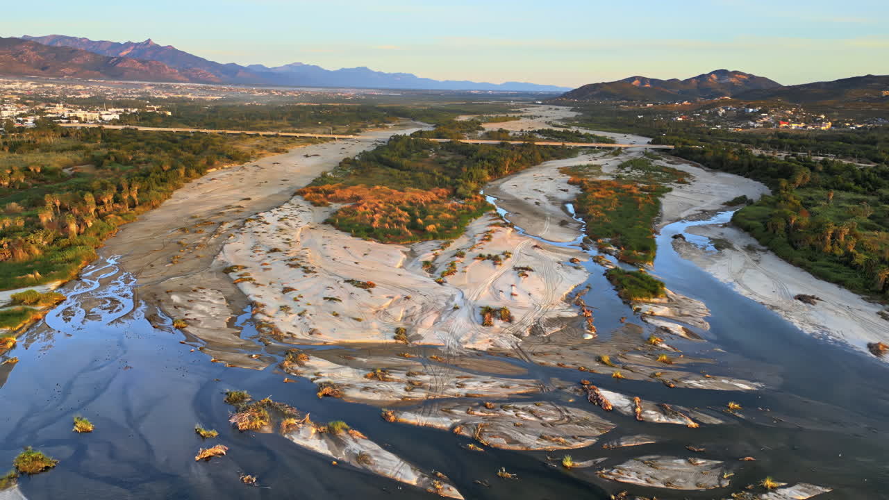 Aerial drone view of a calm river meeting the sea, surrounded by lush green vegetation and distant hills