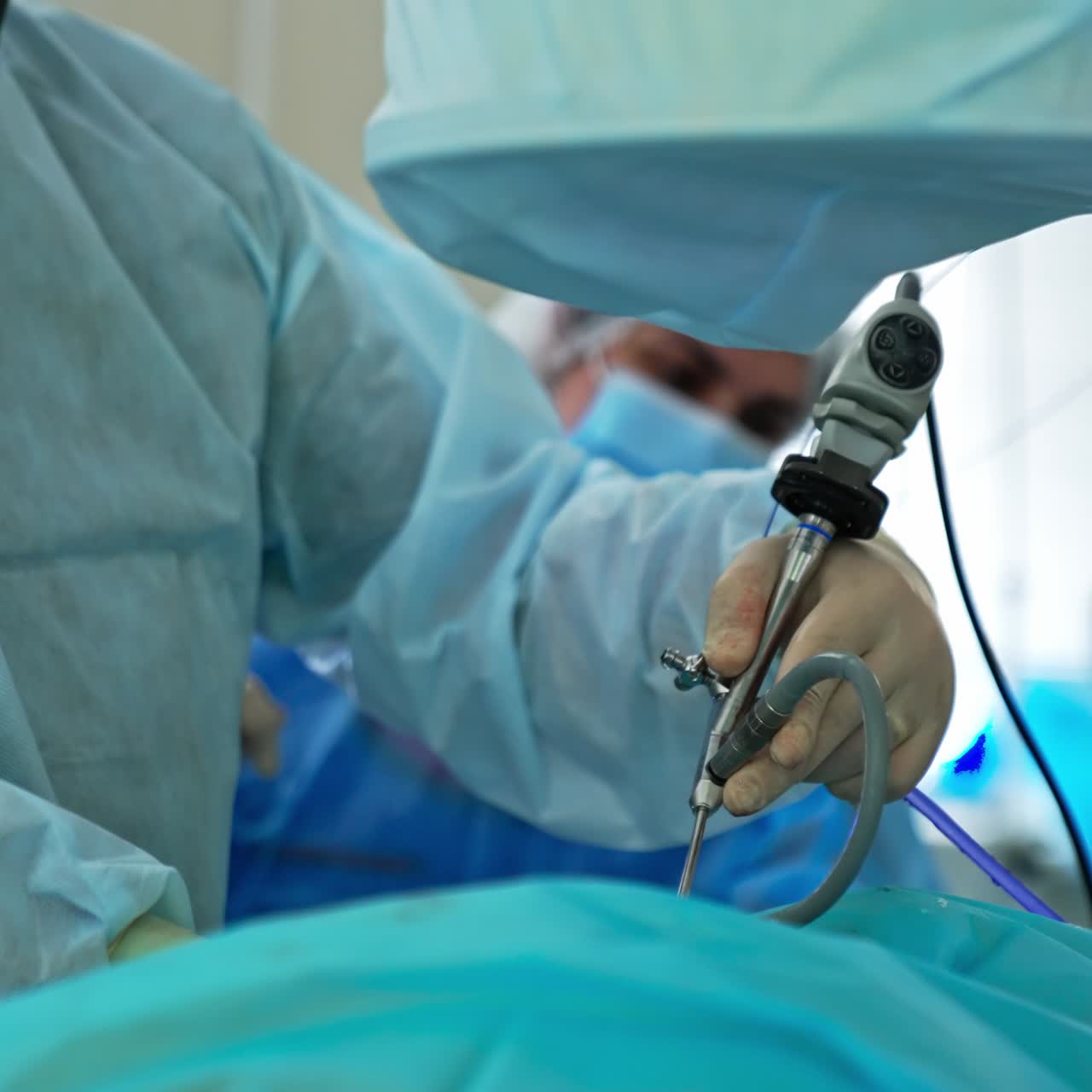 Laparoscopy device being used by a surgeon at operation. Doctor moves the tool slowly and some drops of liquid fall from his hands. Close up. Assistant doctor at the backdrop in blur