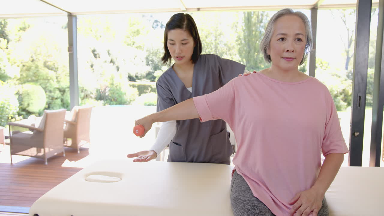 Helping senior asian woman with arm exercise, physical therapist using small ball at home