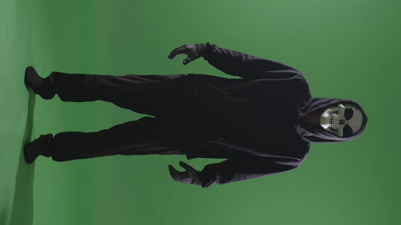 hombre aterrador en la sudadera con capucha usando máscara de halloween de pie en el fondo de la pantalla verde