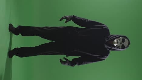 hombre aterrador en la sudadera con capucha usando máscara de halloween de pie en el fondo de la pantalla verde