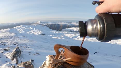 person pouring coffee to wooden mug at idyllic snow covered mountains landscape - slow motion