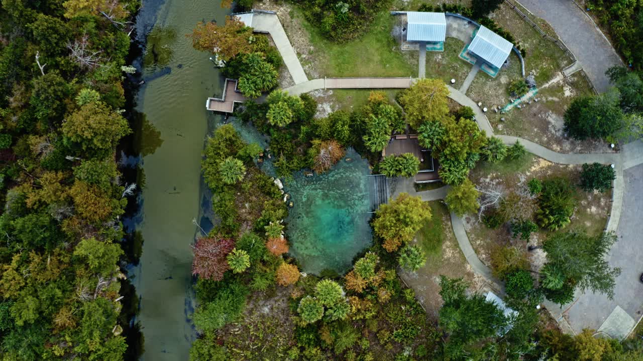 Crystal-blue spring beside a calm river at Pitt and Sylvan Springs, Florida, surrounded by walkways, trees, and small park buildings