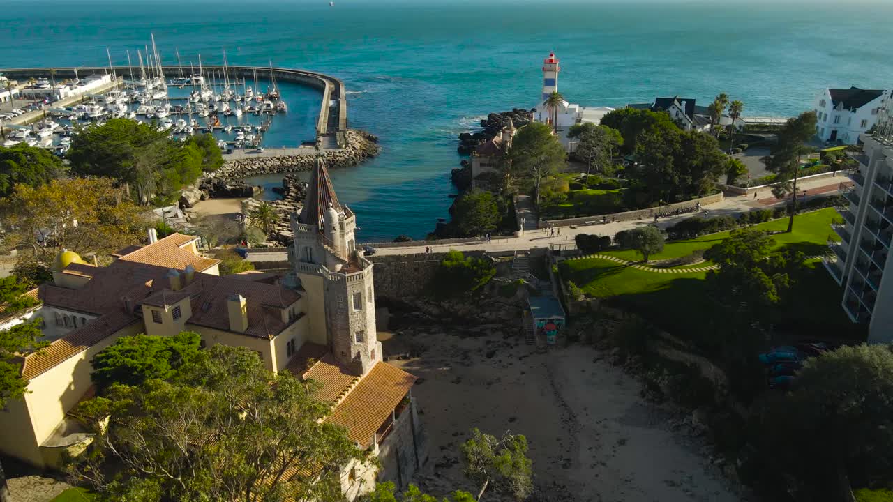 Aerial drone video flying over gorgeous historical view point called Casa de Santa Maria in Cascais Portugal at sunny day, Forte de Santa Marta lighthouse on rocks and reefs near Atlantic ocean beach