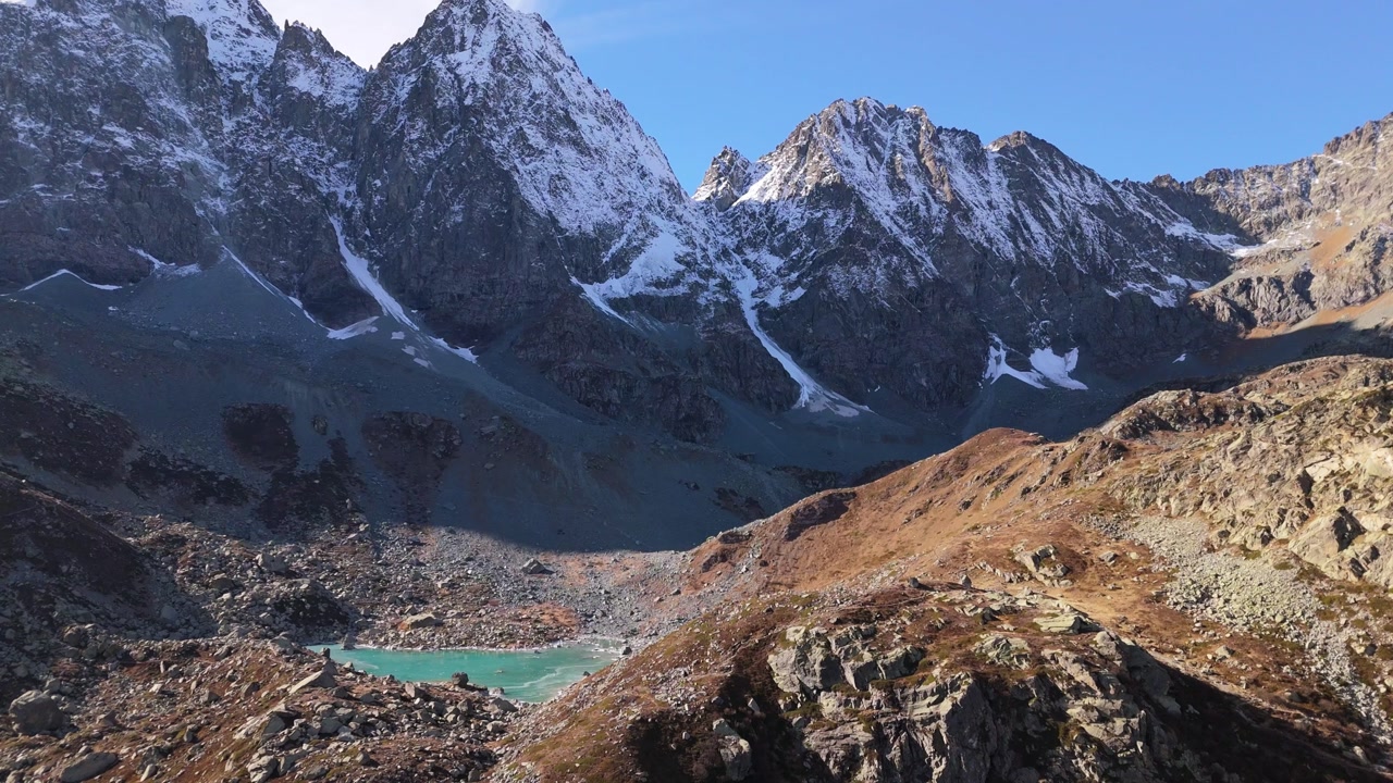 Zoom out revealing Chiaretto lake with turquoise water and dramatic Monviso peaks under clear sky.