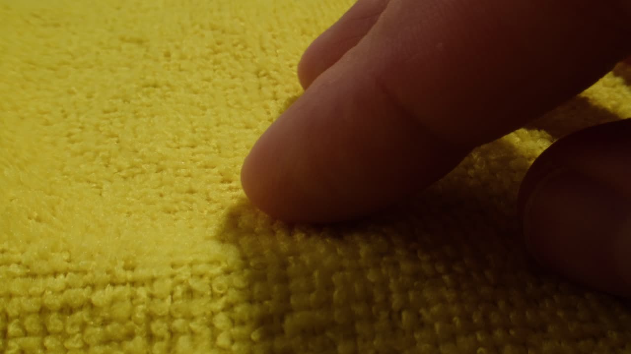 Human Finger Gently Rubbing Yellow Textured Fabric