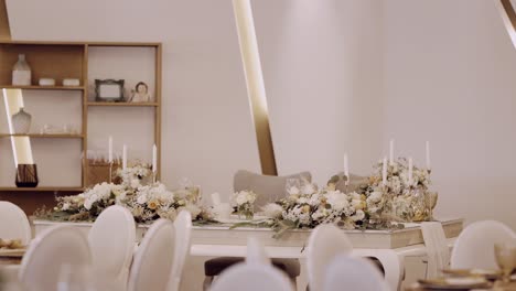 wedding table decorated with floral arrangements, candles, and white chairs in soft lighting