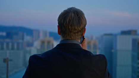 a professional man overlooking the seoul cityscape at sunset turns to reveal an important phone call, captured in a cinematic dolly back, slow-motion shot