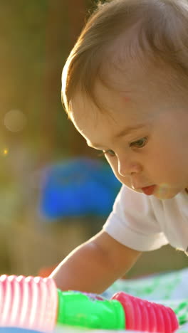 adorable one-year-old boy playing outdoors in the rays of sun. lovely kid waving with a toy hammer. side view. close up. blurred backdrop. vertical video