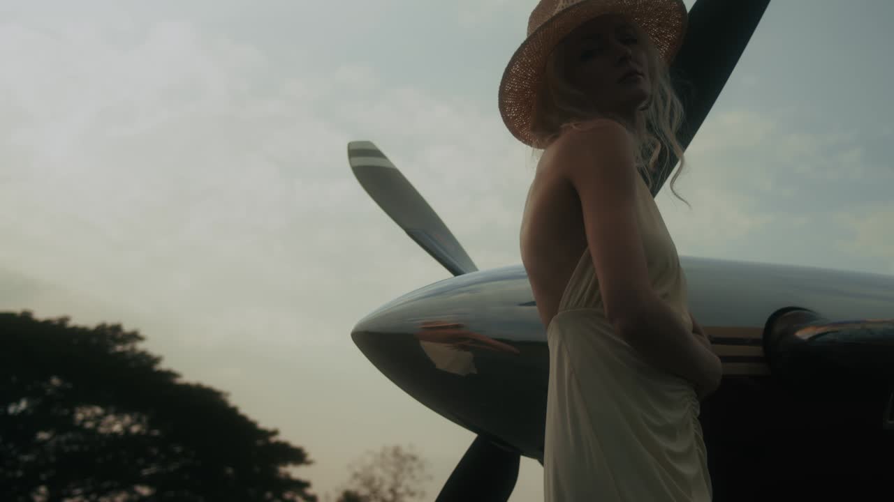 Woman in vintage dress near airplane at sunset