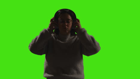 mujer con auriculares inalámbricos transmitiendo música desde un teléfono móvil contra una pantalla verde con iluminación de bajo nivel