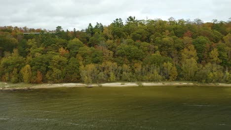 aerial tracking shot of trees along coast with reveal of green bridge during peak fall foliage