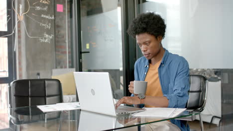 African-american-casual-businessman-using-laptop-and-drinking-coffee-at-desk,-slow-motion