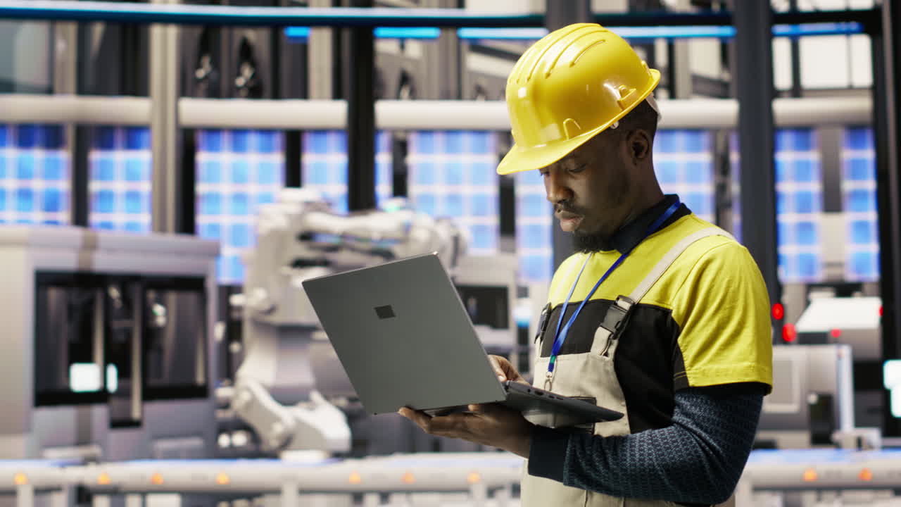 Vertical video Technician in solar panels factory oversees robot assembly lines using laptop