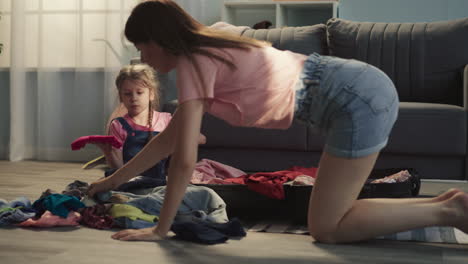 upset little girl looks at mother gathering clothes on floor