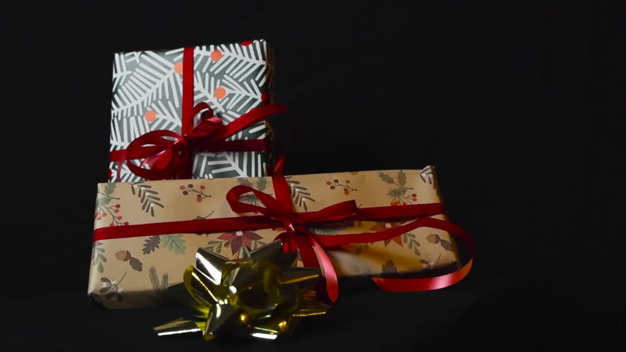 прекрасные кадры медленно уменьшаются или отдаляются от праздников, упакованных в рождественские подарки или подарки, упакованные в красочную и коричневую упаковочную бумагу, завязанные красными лентами на черном фоне