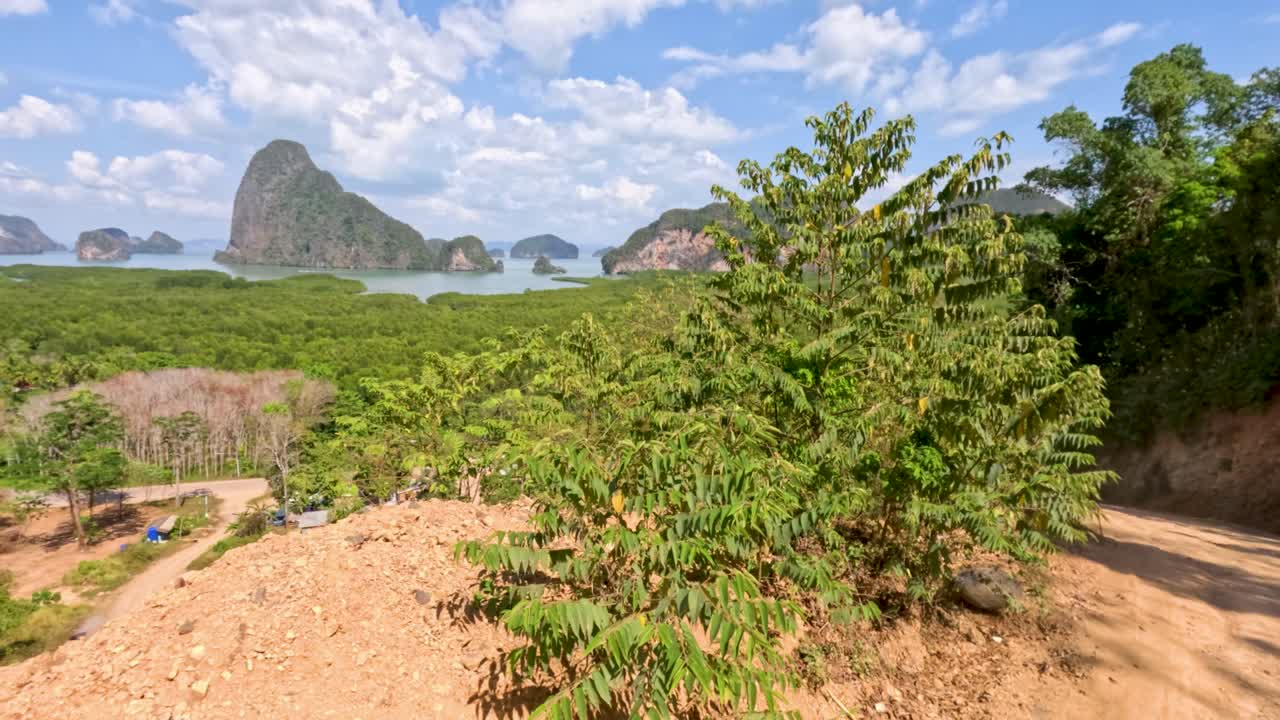 Off-road vehicle drives down dirt road with lush jungle, mangroves, and limestone cliffs in sunlight