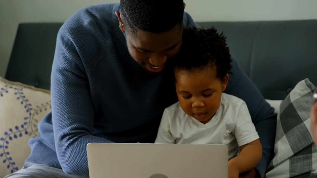 Front view of young black father and son using laptop in living room of comfortable home 4k