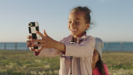 close up portrait of little girls posing taking selfie photo using smartphone playful friend hiding behind enjoying silly fun