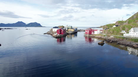 Old-Norwegian-traditional-fishing-village-on-a-nice-calm-summer-day,-while-a-boat-just-left-the-harbor,-Aerial-Forwarding-shot