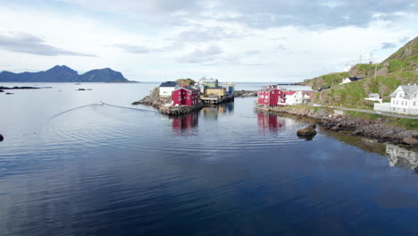 old norwegian traditional fishing village on a nice calm summer day, while a boat just left the harbor, aerial forwarding shot