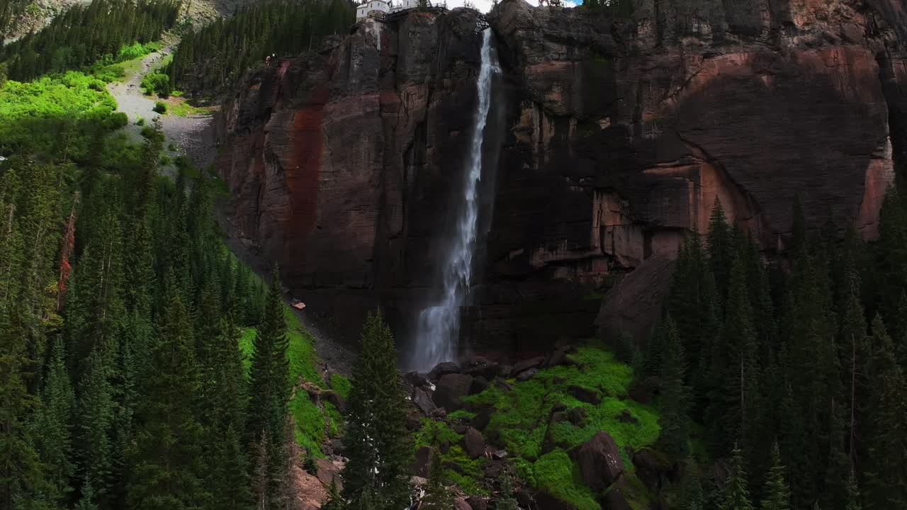 Telluride Bridal Veil Falls aerial drone Waterfall Telluride windy mist spray Black Bear Pass Road Colorado pine tree Ouray Ridgway Box Canyon cliffside 4wd hiking cloudy sun blue sky backwards pan up