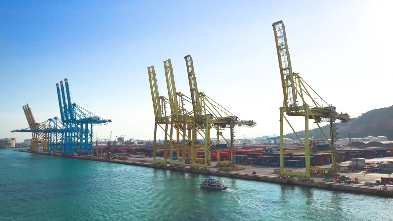 Port przemysłowy z masywnymi dźwigami kontenerowymi wzdłuż nabrzeża, z małą łodzią płynącą po turkusowej wodzie pod czystym błękitnym niebem, symbolizujący globalny handel i żeglugę morską