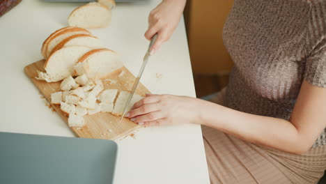 high angle view of youth chopping cake slices into small precise pieces on wooden board over white table, crumbs scattered, soft window light highlighting hands and calm culinary preparation moment