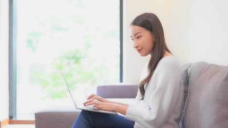 side view woman working on laptop computer smiling at home interior