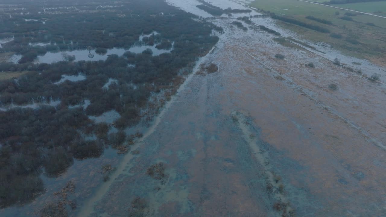 vista aérea de aguas altas, inundación del río durbe, agua marrón y fangosa, campos agrícolas bajo el agua, día de invierno nublado con nieve ligera, disparo de drone de ojo de pájaro avanzando