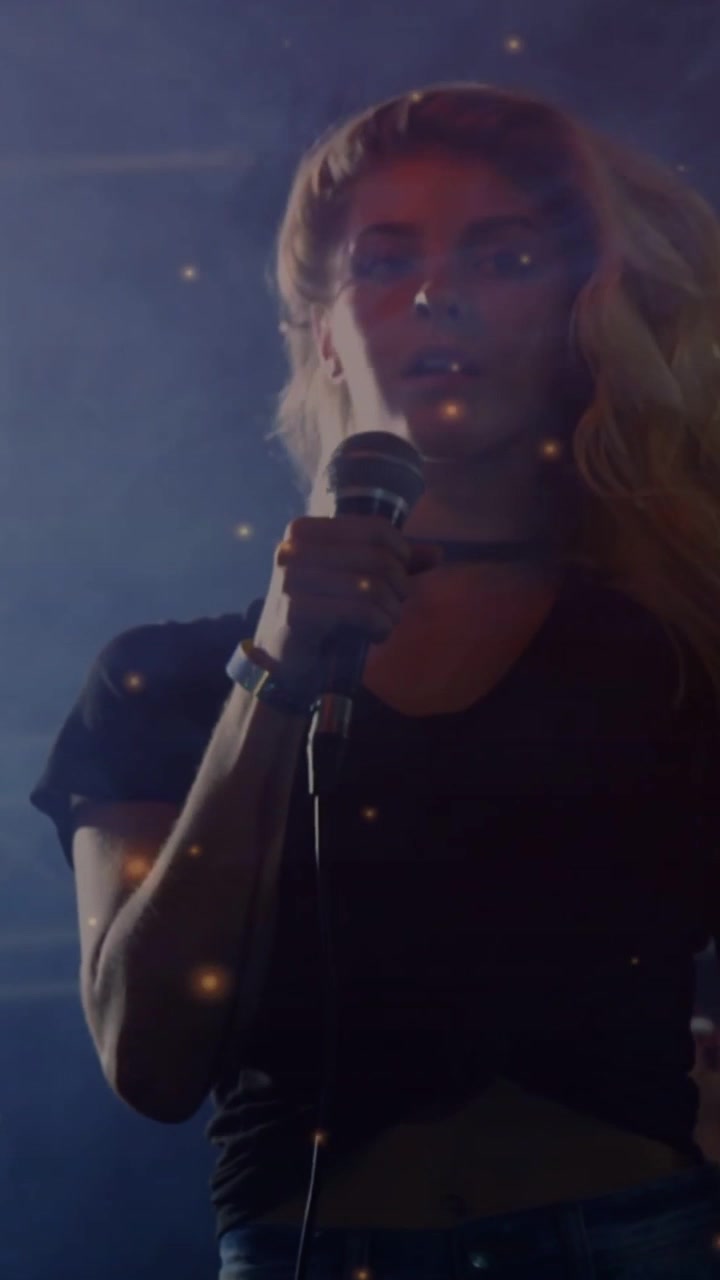 Vertical video: Female singer singing, holding mic, camera tilting up, particles shaping music mood