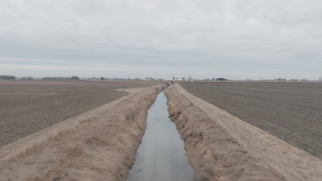 aerial shot of long stretched ditch filled with water cutting through dry, grassy field.